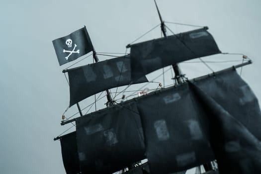 Close-up details of Pirate ship model Black pearl made of plywood. Flag Jolly Roger Skull and bones in focus, partially blurred patched sails and ropes