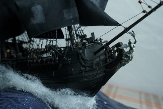 Pirate ship model Black pearl made of plywood, with miniature figures of pirate sailors, close-up details. Bow with figure of woman with wings. Ship sails on waves with patched sails