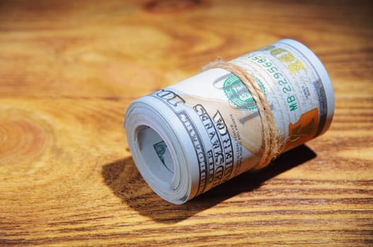 A roll of dollars on a wooden textured table in the dark illuminated by a ray of light