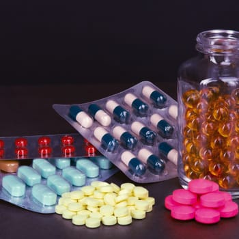 Pills and tablets of different colors are scattered and in bottles on a dark background