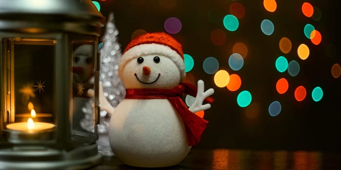 Christmas composition: a snowman, a lantern with candles and blurred bokeh lights in the background.