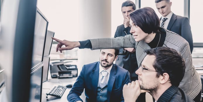 Business team looking at data on multiple computer screens in corporate office. Businesswoman pointing on screen. Business people trading online. Business, entrepreneurship and team work concept.