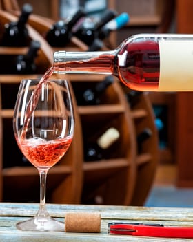 Winery. Pouring rose wine from the bottle into the wine glass for tasting, on a rustic wooden table. Beverage, alcohol.