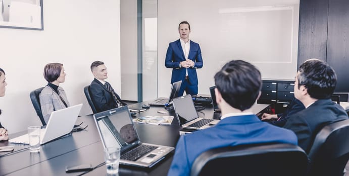 Successful team leader and business owner leading informal in-house business meeting. Businessman working on laptop in foreground. Business and entrepreneurship concept.