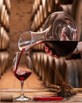 Winery. Pouring red wine from the decanter into the wine glass for tasting, on a rustic wooden table. Beverage, alcohol.