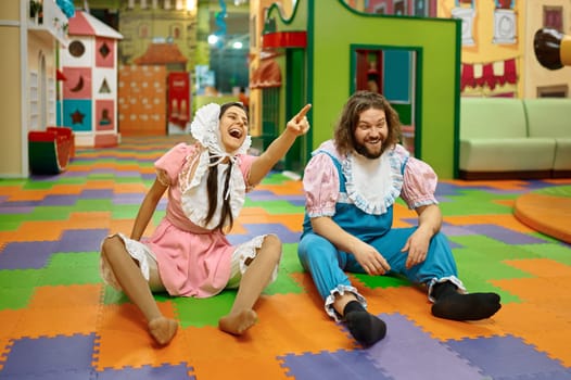 Funny man and woman wearing like newborn babies sitting on playroom floor