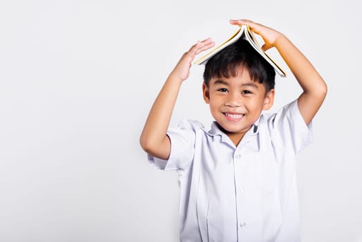 Asian adorable toddler smiling happy wearing student thai uniform red pants stand holding book over head like roof in studio shot isolated on white background, Portrait little children boy preschool