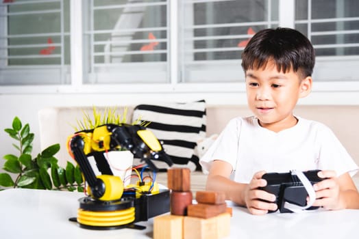 Happy Asian little kid boy using remote control playing robotic machine arm for pick up wood block, Funny child learning successful getting lesson control robot arm, Technology science education