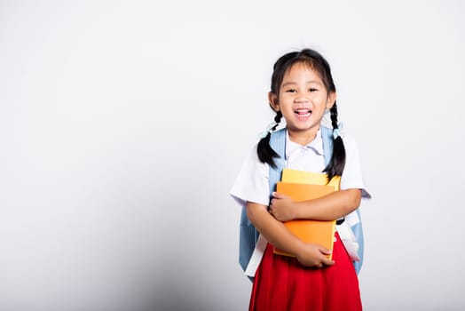 Asian adorable toddler smiling happy wear student thai uniform red skirt stand hold or hugging book in studio shot isolated on white background, Portrait little children girl preschool, Back to school