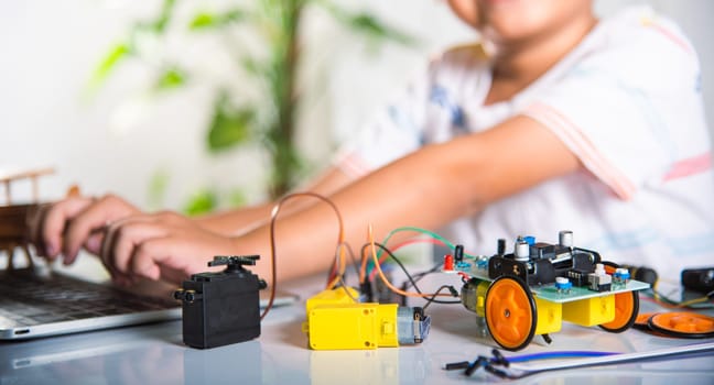 Asian kid boy learns coding and programming with laptop for Arduino robot car, Little child students typing code in computer online with car toy, STEAM education AI technology future course learning