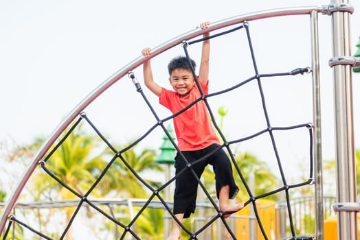 Asian child smiling playing climbing outdoor playground, happy preschool little kid having funny while playing climbs on a rope climbing net on playground equipment in daytime in summer, Little boy