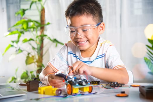 Little child remotely learn online with car toy before sent code, Asian kid boy plugging energy and signal cable to sensor chip with Arduino robot car, STEAM education AI technology course learning