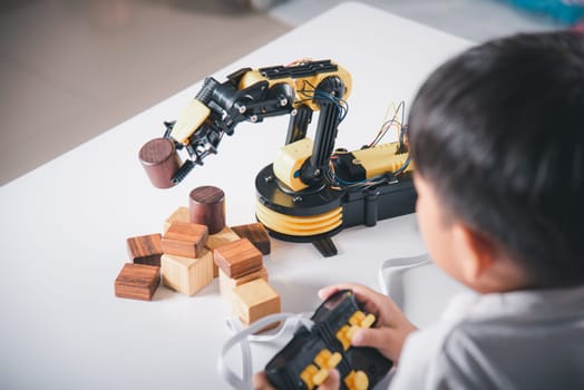 Happy Asian little boy using remote control playing robotic machine arm for pick up wood block, Funny learning successful getting a lesson control robot arm, Technology science education concept