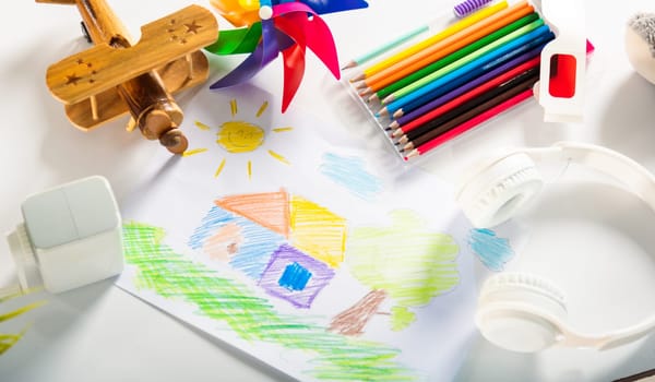 Child colorful drawing landscape my home dream on white paper, kid preschooler draw country house picture with pencil on table, arts homework concept