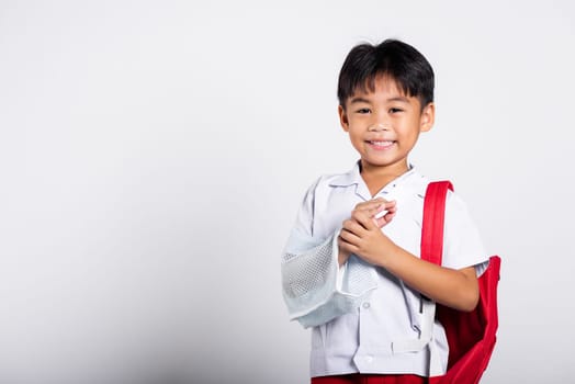 Asian student kid boy wearing student thai uniform accident broken bone wearing splint arm plaster fiberglass cast covering arm in cast at studio shot isolated on white background, back to school