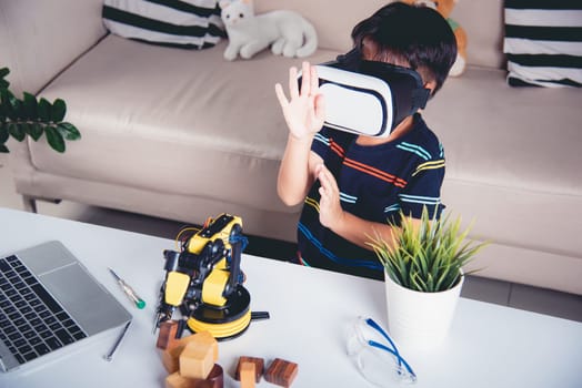 Virtual Reality Simulator. Asian kid boy using VR glasses on robotic arm in workshop, Child learning programer control robot arm with sensors to pick up wood block, Technology education. industry 4.0