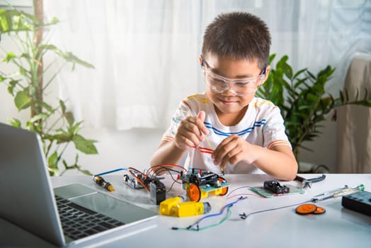Asian kid boy assembling the Arduino robot car homework project at home, Little child tighten the nut with a screwdriver to assemble car toy, creating electronic AI technology workshop school lesson