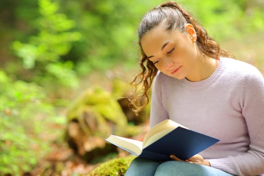 Concentrated woman reading a paper book sitting in nature