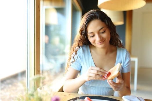 Front view of a happy woman spreading tomato on bread sitting in a restaurant