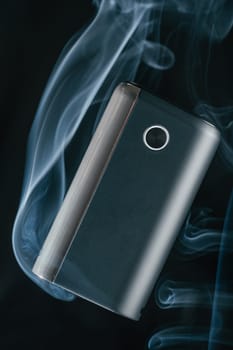 Black new GLO heating smoking device floats in puffs of white blue neon smoke. Modern electronic cigarettes