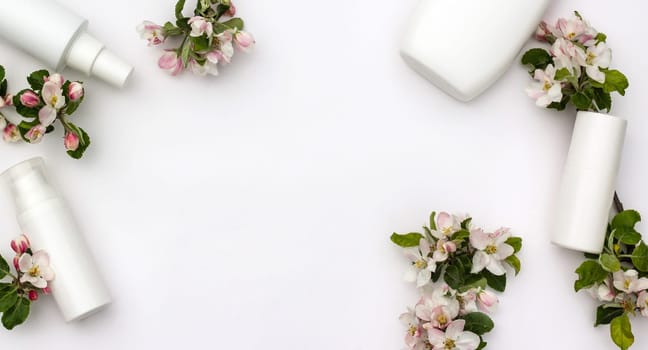 White cosmetic bottles with pear flowers on a white background. Natural organic cosmetics concept. Banner