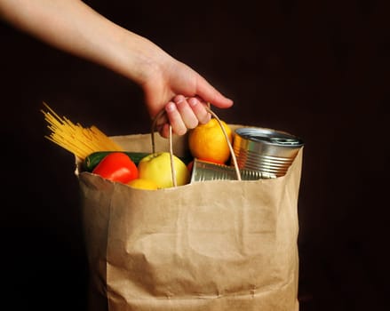 Boy holds paper bag with products on a brown background. A child takes food from the food delivery service. Canned food, pasta, vegetables, fruits. Contactless delivery.