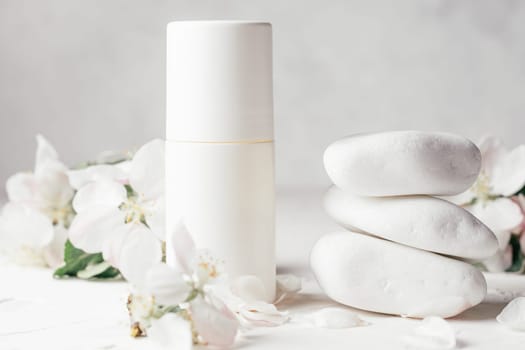 Antiperspirant roll-on deodorant near stack of white pebble stones on light plaster surface with apple flowers