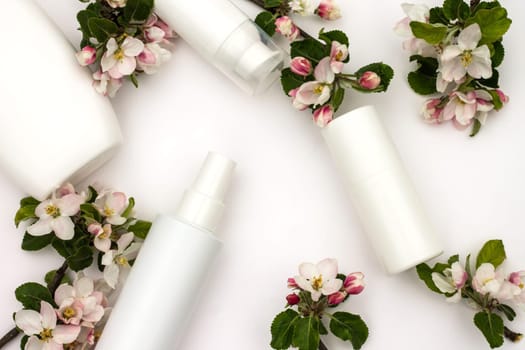 White cosmetic bottles with pear flowers on a white background. Natural organic cosmetics concept.