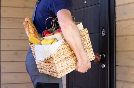 Fresh organic bread, vegetables, greens and fruits, cereals and pasta in a wicker basket in the hands of a bicycle courier. Bike eco-friendly delivery or donation of ecological farm food concept.