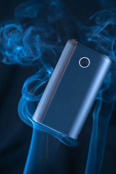 Black new GLO heating smoking device floats in puffs of white blue neon smoke. Modern electronic cigarettes