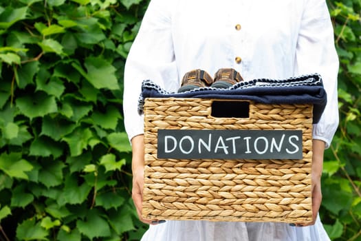 Female hands holding a box for clothing donations on a greenery background. Charity and donation concept, copy space.