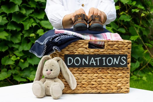 Hands putting a children shoes in a box for clothing donations on a greenery background. Charity and donation concept, copy space.