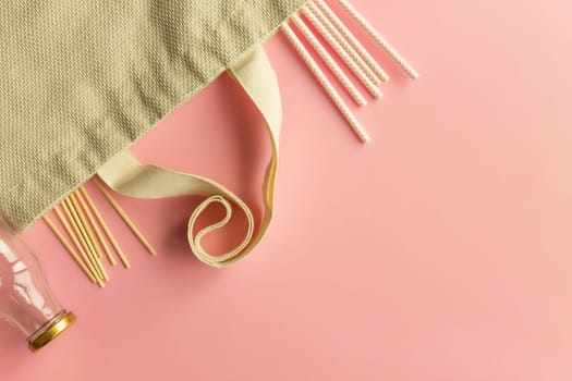 Fabric cotton shopping bags, glass bottles and jars, paper straws and wooden sticks on a pink background. Zero waste and ecological concept. Top view. Copy space.