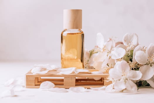 Cosmetic, aroma or massage oil on wooden podium in form of pallet on light plaster surface with apple flowers