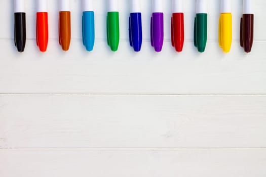 Multi-colored markers on a white wooden background. Top view. Copy space