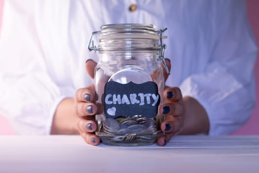 Woman hands holding a glass jar with coins with a chalk Charity tag, donation and charity concept