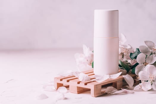 Antiperspirant roll-on deodorant on wooden podium in form of pallet on light plaster surface with apple flowers. Copy space