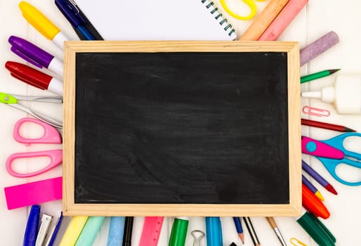 Back to school black chalk board on a white wooden background, color supplies. Top view. Copy space. Education concept