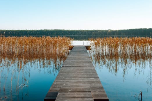 Picturesque landscape of Lake Baltieji Lakajai in Labanoras Regional Park, Lithuania. A wooden empty pier among blue water, reeds and a forest on the opposite bank