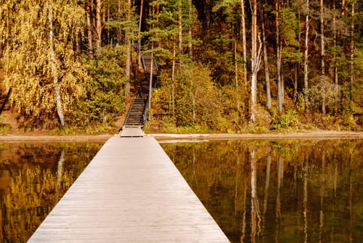Wooden pier, autumn forest and wooden stairs up to a hill on Lake Baltieji Lakajai in Labanoras Regional Park, Lithuania.