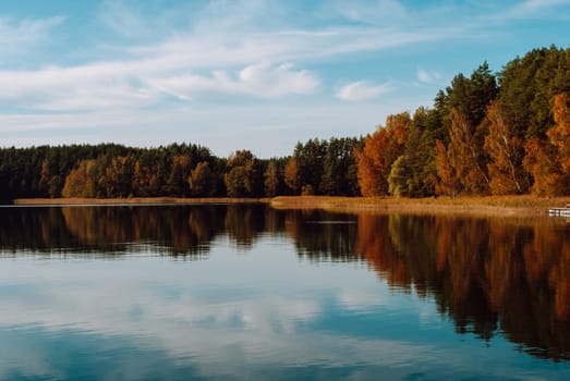 Autumn multi-colored mixed forest and sky with clouds is reflected in the surface of the water of Lake Baltieji Lakajai in Labanoras Regional Park, Lithuania.