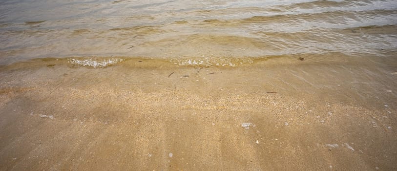 Clear sea water and small waves and ripples crossing a sandy beach and shellgrit as the tide comes in on the foreshores of Hervey bay, Queensland.