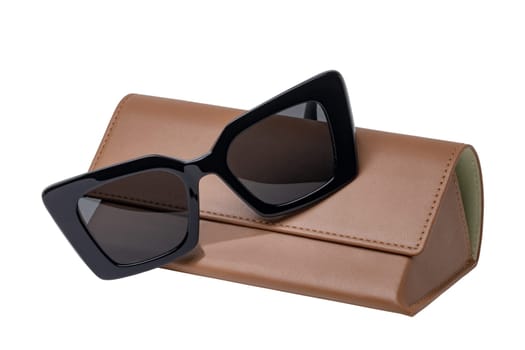 Summer glasses fashion. Female elegant trendy luxury black sun glasses resting on a brown leather case isolated on a white background. Clipping path. Macro.