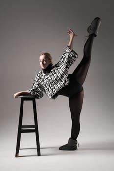 Ballet dancer woman black dress on gray background, Ballerina posing and showing her flexibility on gray background in studio with chair. Text on sweater DREAMS OF.