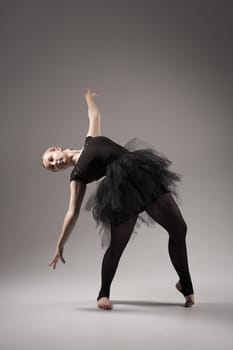 Ballerina Dancing with tutu Modern Ballet Dancer in dancer tutu, Gray Background. Dancer in Black clothes showing her flexibility posing on gray background in studio.