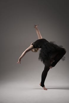 Ballerina Dancing with tutu Modern Ballet Dancer in dancer tutu, Gray Background. Dancer in Black clothes showing her flexibility posing on gray background in studio.