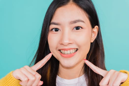 Asian beautiful young woman teen pointing finger to teeth, portrait of happy Thai female confident smiling show white teeth, studio shot isolated on blue background, Dental health care concept