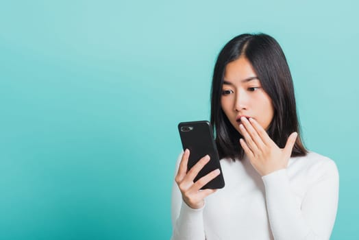 Portrait female anxious scared on the phone seeing bad news, Young beautiful Asian woman surprised shocked with mobile phone close mouth with palm, studio shot isolated on a blue background