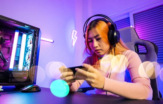 Losing. Gamer in playing video game online with smartphone with neon lights she fail game over, confused Asian woman wearing gaming headphones play mobile phone feeling shocked disappointed at home