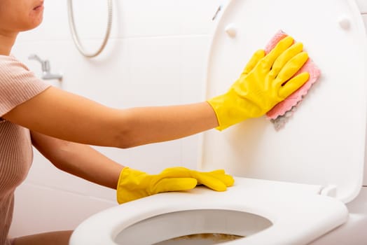 Woman cleaning toilet seat by pink cloth wipe restroom, female wearing yellow rubber gloves she sitting and clean the bathroom, Housekeeper healthcare concept
